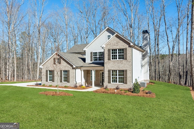 view of front of house featuring brick siding, a chimney, a front yard, and cooling unit