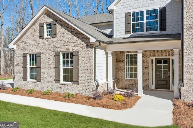 view of exterior entry featuring brick siding and a shingled roof