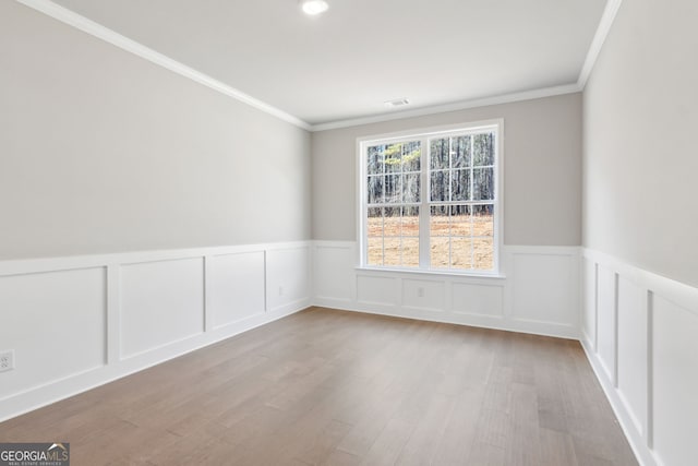 spare room with a wainscoted wall, crown molding, visible vents, and wood finished floors