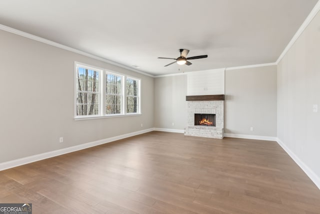 unfurnished living room featuring crown molding, dark wood-type flooring, a ceiling fan, a brick fireplace, and baseboards