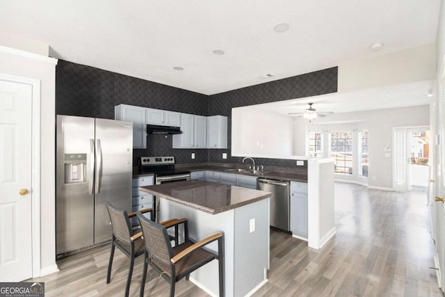 kitchen with ceiling fan, kitchen peninsula, a kitchen bar, a kitchen island, and appliances with stainless steel finishes