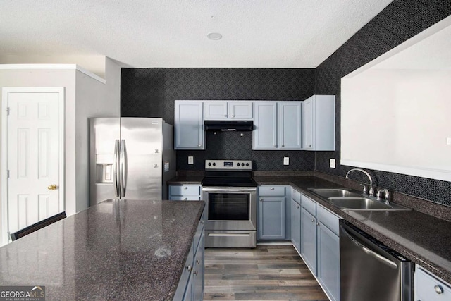 kitchen with sink, dark stone countertops, a textured ceiling, appliances with stainless steel finishes, and dark hardwood / wood-style flooring