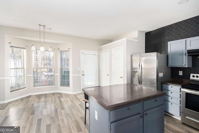 kitchen with appliances with stainless steel finishes, backsplash, wood-type flooring, decorative light fixtures, and a center island