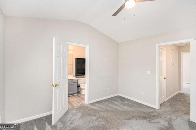 unfurnished bedroom featuring ensuite bath, ceiling fan, light colored carpet, and lofted ceiling