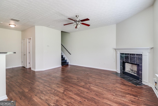 unfurnished living room with a tile fireplace, a textured ceiling, ceiling fan, and dark hardwood / wood-style flooring