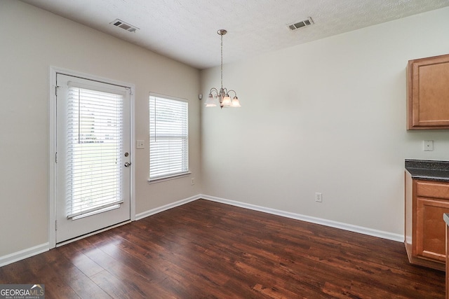 unfurnished dining area with a textured ceiling, an inviting chandelier, and dark hardwood / wood-style floors