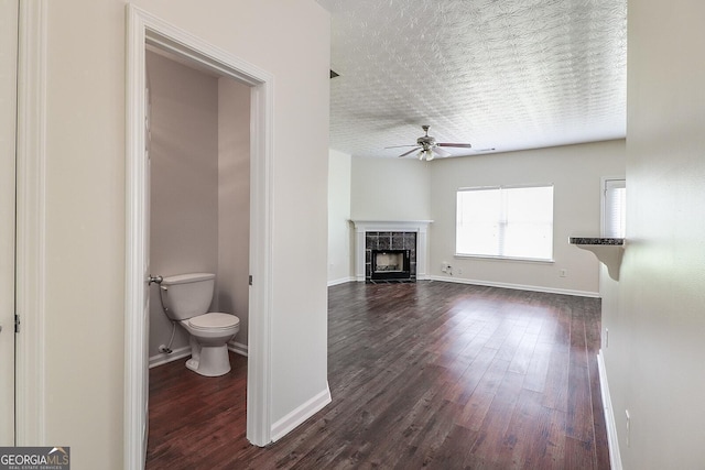 unfurnished living room featuring a tiled fireplace, ceiling fan, and dark hardwood / wood-style floors