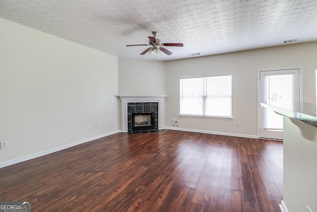 unfurnished living room featuring dark hardwood / wood-style flooring, a tile fireplace, a textured ceiling, and ceiling fan