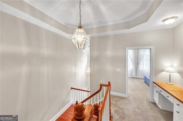 hall with light colored carpet, a notable chandelier, a raised ceiling, and ornamental molding