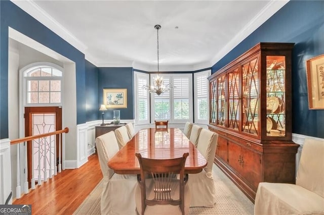 dining space with light hardwood / wood-style flooring, ornamental molding, and an inviting chandelier