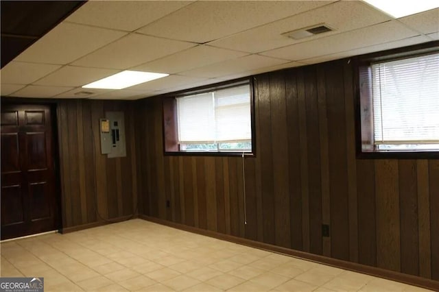 unfurnished room featuring electric panel, wooden walls, and a drop ceiling