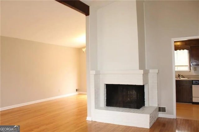 unfurnished living room with a fireplace, beamed ceiling, light hardwood / wood-style floors, and sink