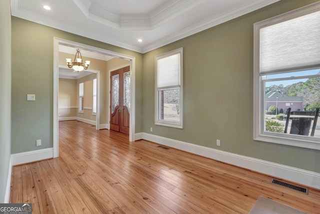 entryway featuring a notable chandelier, a raised ceiling, ornamental molding, and light hardwood / wood-style flooring