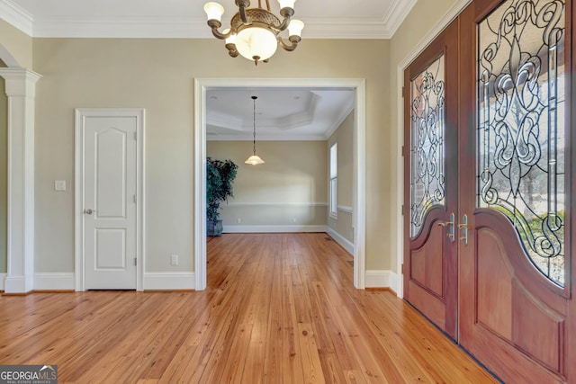 foyer entrance featuring ornate columns, light wood-type flooring, a notable chandelier, and ornamental molding