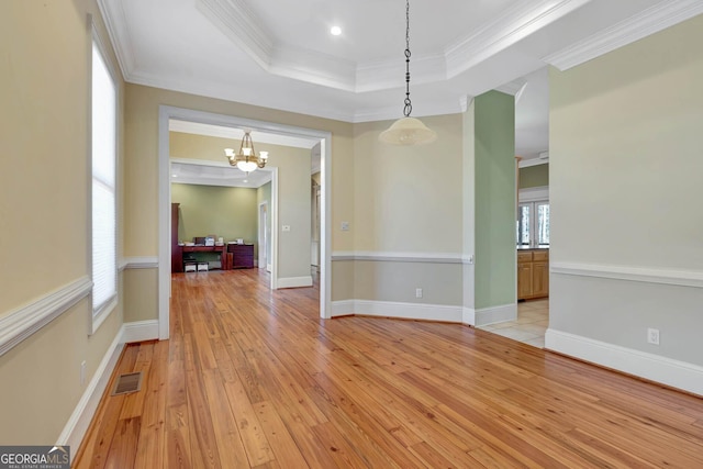 spare room with a raised ceiling, an inviting chandelier, light hardwood / wood-style floors, and ornamental molding