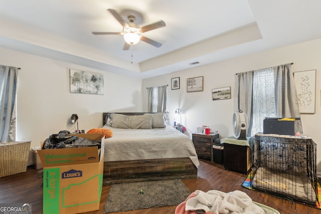 bedroom featuring dark hardwood / wood-style flooring, a tray ceiling, and ceiling fan