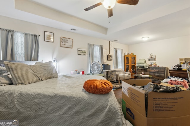 bedroom with ceiling fan, a raised ceiling, and multiple windows