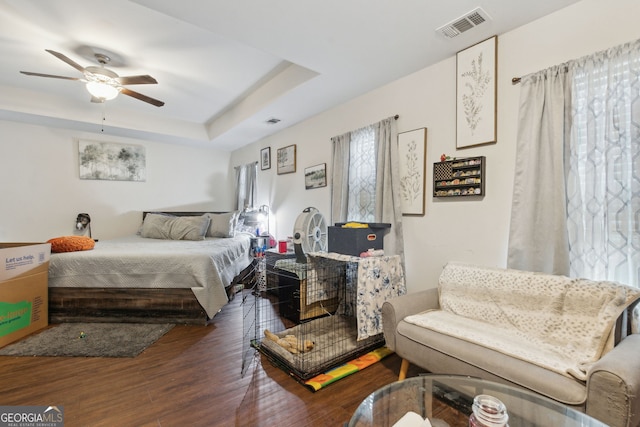 bedroom with dark hardwood / wood-style flooring, ceiling fan, and a raised ceiling