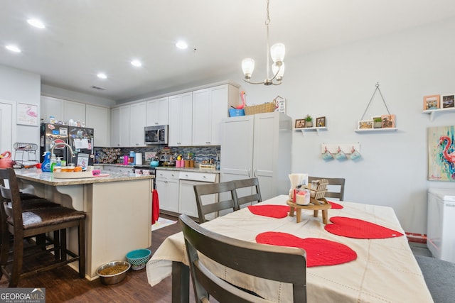 kitchen with backsplash, a kitchen island with sink, a kitchen breakfast bar, hanging light fixtures, and white cabinetry