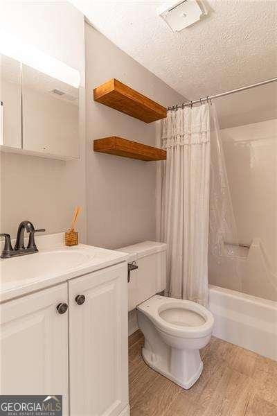 full bathroom featuring vanity, a textured ceiling, shower / bathtub combination with curtain, hardwood / wood-style floors, and toilet