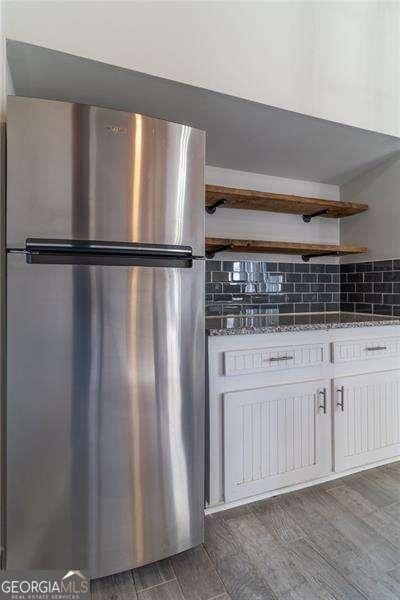 kitchen with stainless steel fridge, backsplash, dark stone counters, dark hardwood / wood-style floors, and white cabinetry