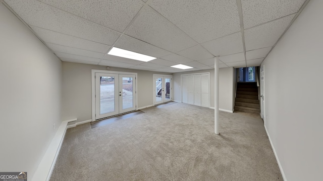 basement with a drop ceiling, light colored carpet, and french doors