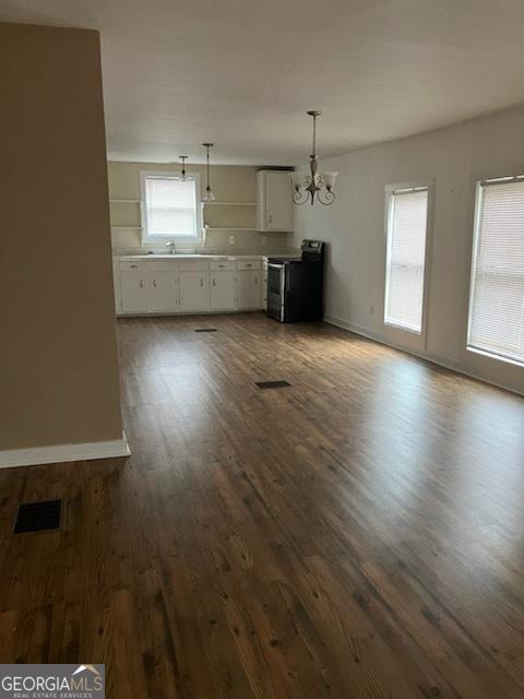 unfurnished living room featuring a chandelier, sink, and dark wood-type flooring