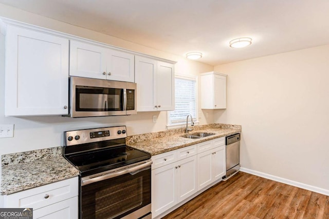 kitchen featuring light stone countertops, appliances with stainless steel finishes, light wood-type flooring, sink, and white cabinets