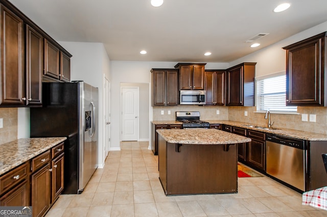 kitchen with light stone counters, a kitchen island, a sink, visible vents, and appliances with stainless steel finishes
