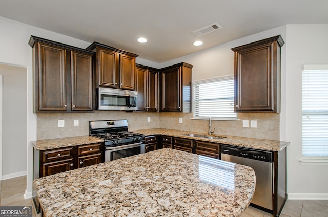 kitchen featuring light stone countertops, appliances with stainless steel finishes, dark brown cabinets, and sink