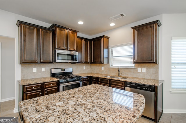 kitchen featuring appliances with stainless steel finishes, a sink, dark brown cabinets, and light stone countertops