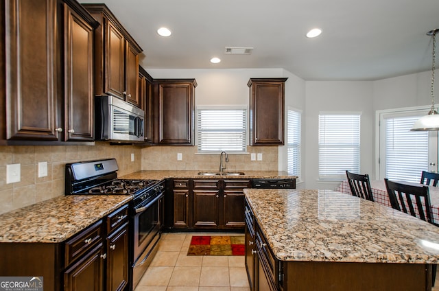 kitchen featuring light stone counters, decorative light fixtures, stainless steel appliances, visible vents, and a sink