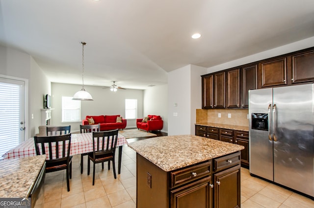 kitchen featuring a center island, stainless steel refrigerator with ice dispenser, hanging light fixtures, open floor plan, and dark brown cabinetry