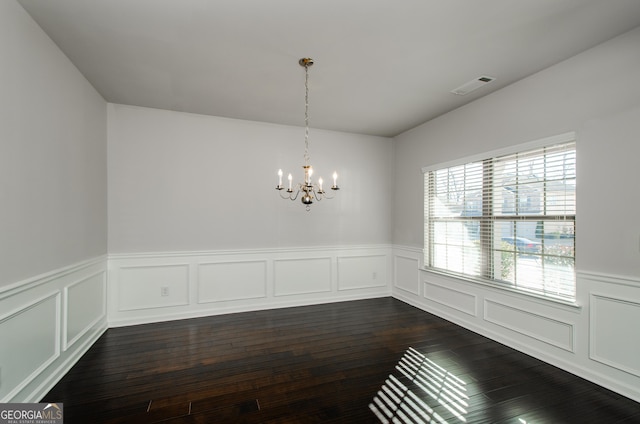 unfurnished dining area with dark wood-style floors, a notable chandelier, visible vents, a decorative wall, and wainscoting