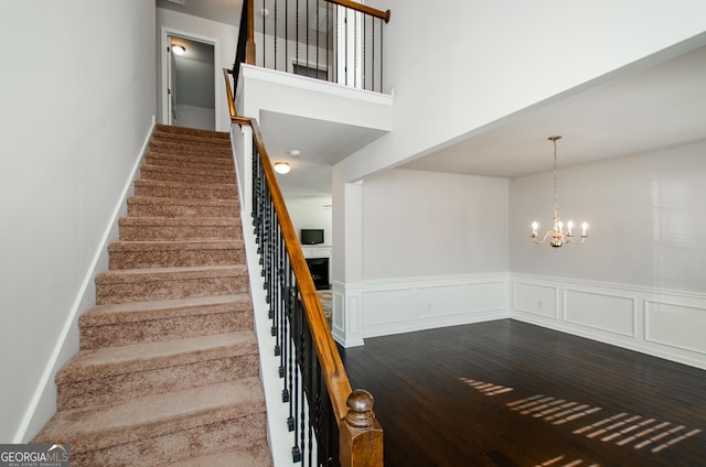 staircase with a chandelier, wainscoting, a decorative wall, and wood finished floors