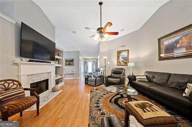 living room with vaulted ceiling, ceiling fan, built in features, light hardwood / wood-style flooring, and a premium fireplace