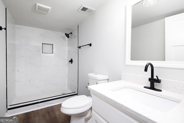 bathroom with a tile shower, hardwood / wood-style flooring, vanity, toilet, and a textured ceiling