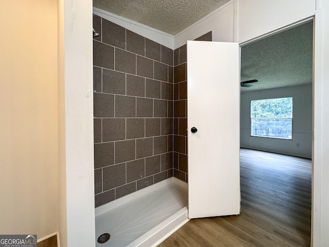 bathroom featuring hardwood / wood-style flooring, ceiling fan, tiled shower, and a textured ceiling