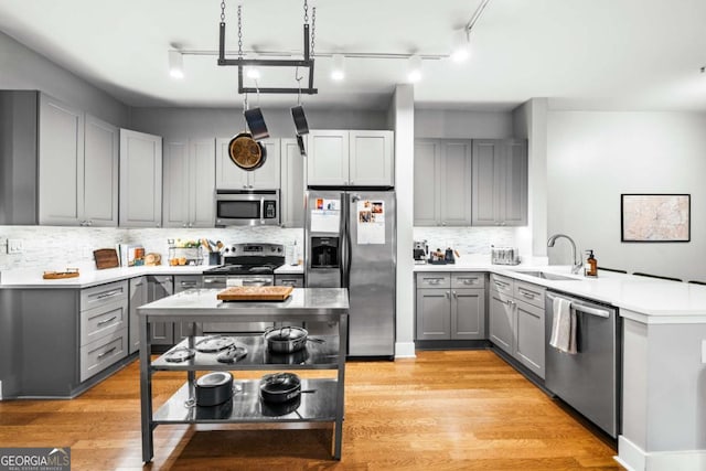 kitchen featuring gray cabinetry, sink, stainless steel appliances, tasteful backsplash, and light hardwood / wood-style flooring