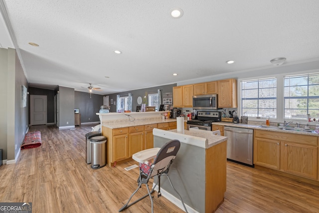 kitchen with ceiling fan, sink, stainless steel appliances, light hardwood / wood-style flooring, and kitchen peninsula