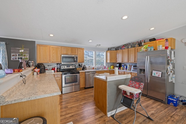 kitchen with kitchen peninsula, light hardwood / wood-style floors, a textured ceiling, appliances with stainless steel finishes, and ornamental molding