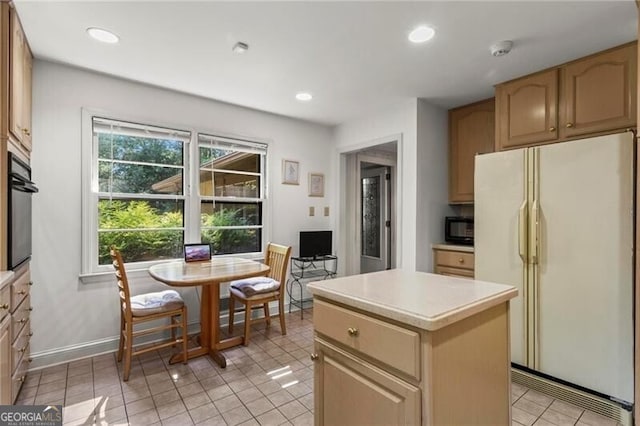 kitchen with a center island, light brown cabinets, light tile patterned floors, white fridge, and oven