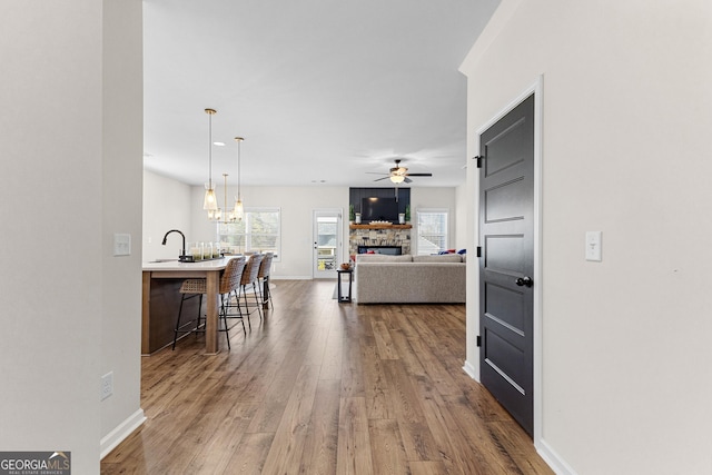 interior space with decorative light fixtures, a breakfast bar, ceiling fan, wood-type flooring, and a stone fireplace