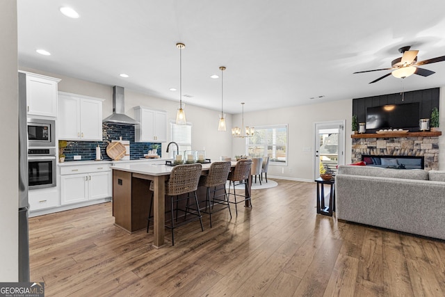 kitchen with stainless steel appliances, white cabinets, an island with sink, and wall chimney exhaust hood