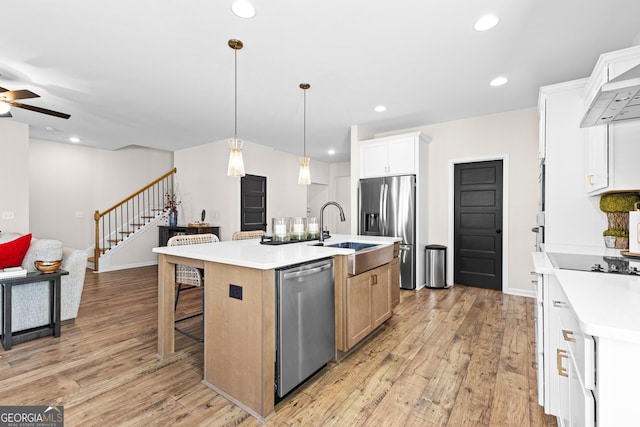 kitchen with hanging light fixtures, an island with sink, white cabinets, appliances with stainless steel finishes, and sink