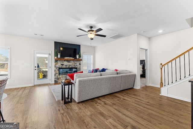 living room featuring ceiling fan, a stone fireplace, and wood-type flooring