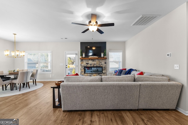 living room with ceiling fan with notable chandelier, wood-type flooring, and a stone fireplace