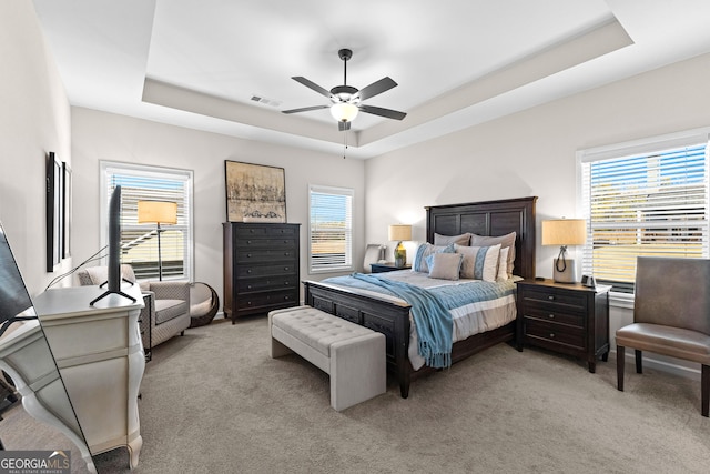 bedroom featuring ceiling fan, a tray ceiling, and light carpet