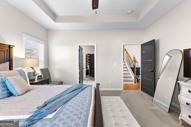 bedroom with a walk in closet, a raised ceiling, and light colored carpet