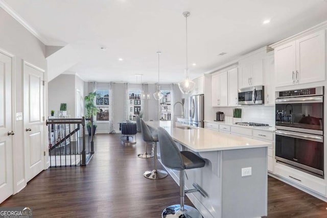 kitchen with stainless steel appliances, decorative light fixtures, a kitchen bar, a center island with sink, and white cabinets